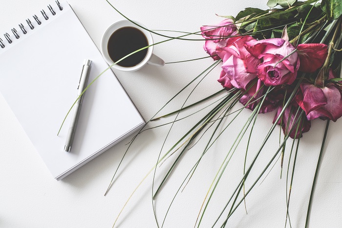 bouquet-de-fleurs-rose-rouge-sur-une-surface-blanche-avec-bloc-blanc-stylo-et-tasse-de-cafe