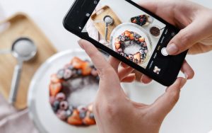 mains tenant un smartphone en train de photographier une couronne de fruits rouges