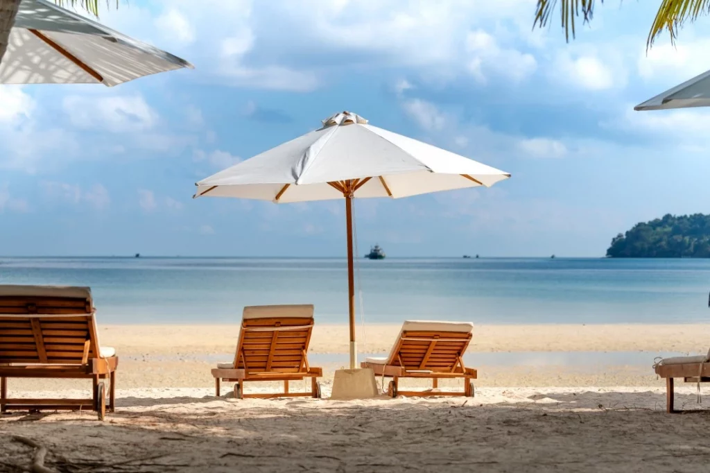 plage-sable-parasol-blanc-trois-chaises-longues- mer-bleue-au-loin
