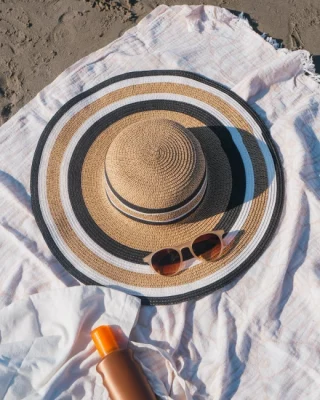 creme-solaire-chapeau-lunettes-sur-drap-de-plage-blanc
